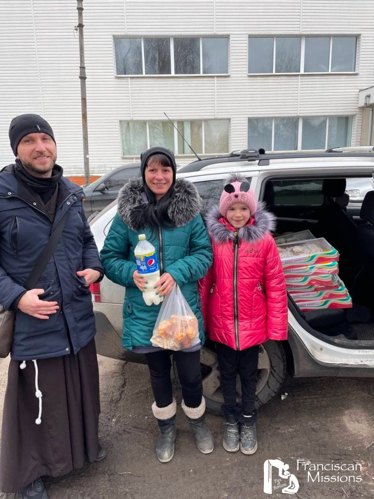 A Franciscan brother giving food to a mother and daughter as part of the relief for Ukraine.
